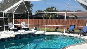 A covered outdoor swimming pool with lounge chairs and a wooden fence in the background. - Charming Coastal Vibe, 3BR Home with Heated Pool (Cape Coral)