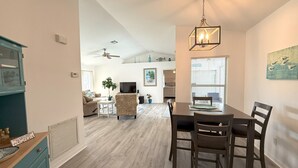 A spacious living area with a dining table, chairs, a television, and a ceiling fan. - Charming Coastal Vibe, 3BR Home with Heated Pool (Cape Coral)