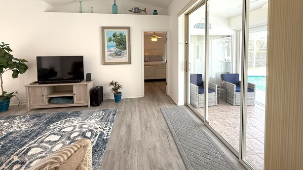 A living room with a TV, a painting, and a potted plant. - Charming Coastal Vibe, 3BR Home with Heated Pool (Cape Coral)