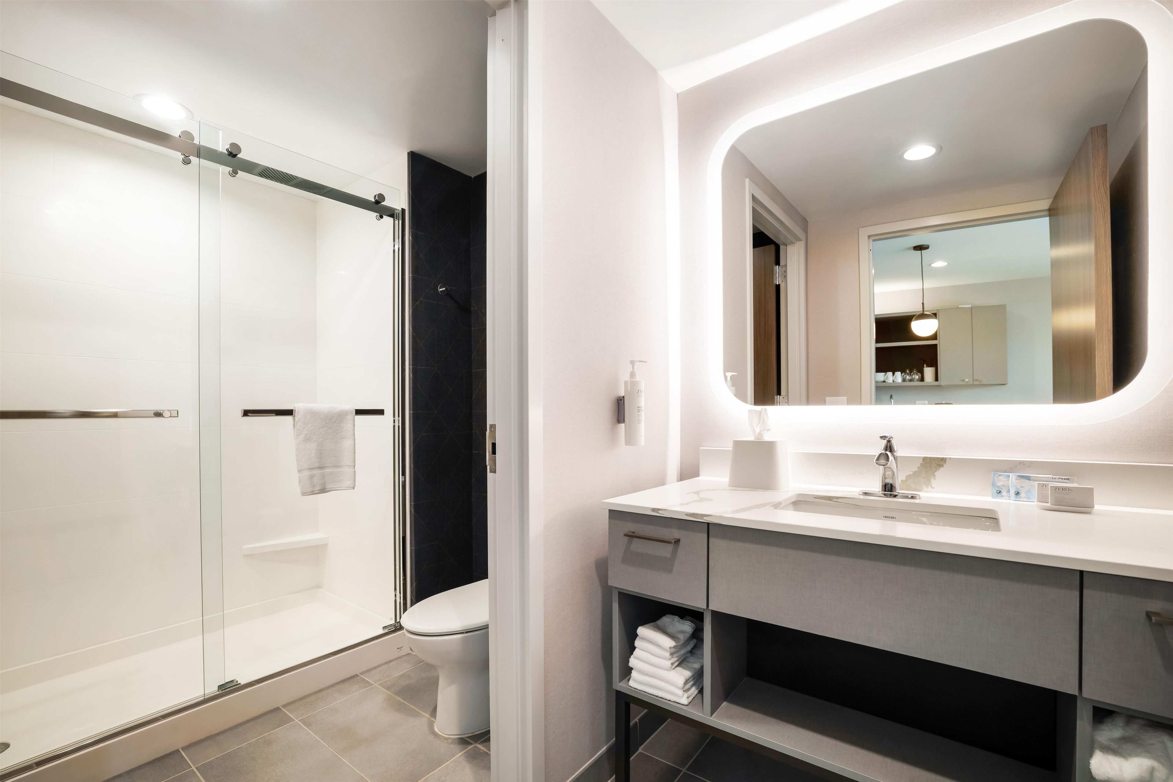 A modern bathroom with a glass shower enclosure, a white sink with a mirror, and a towel rack.