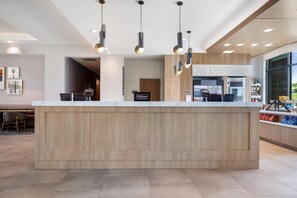 A hotel reception area with a wooden reception desk, a minibar, and a 'SUITE SHOP' sign. - Homewood Suites By Hilton Madison Huntsville (Madison)