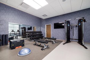 Un gimnasio con equipo de ejercicio, una banca, mancuernas y un televisor montado en la pared.