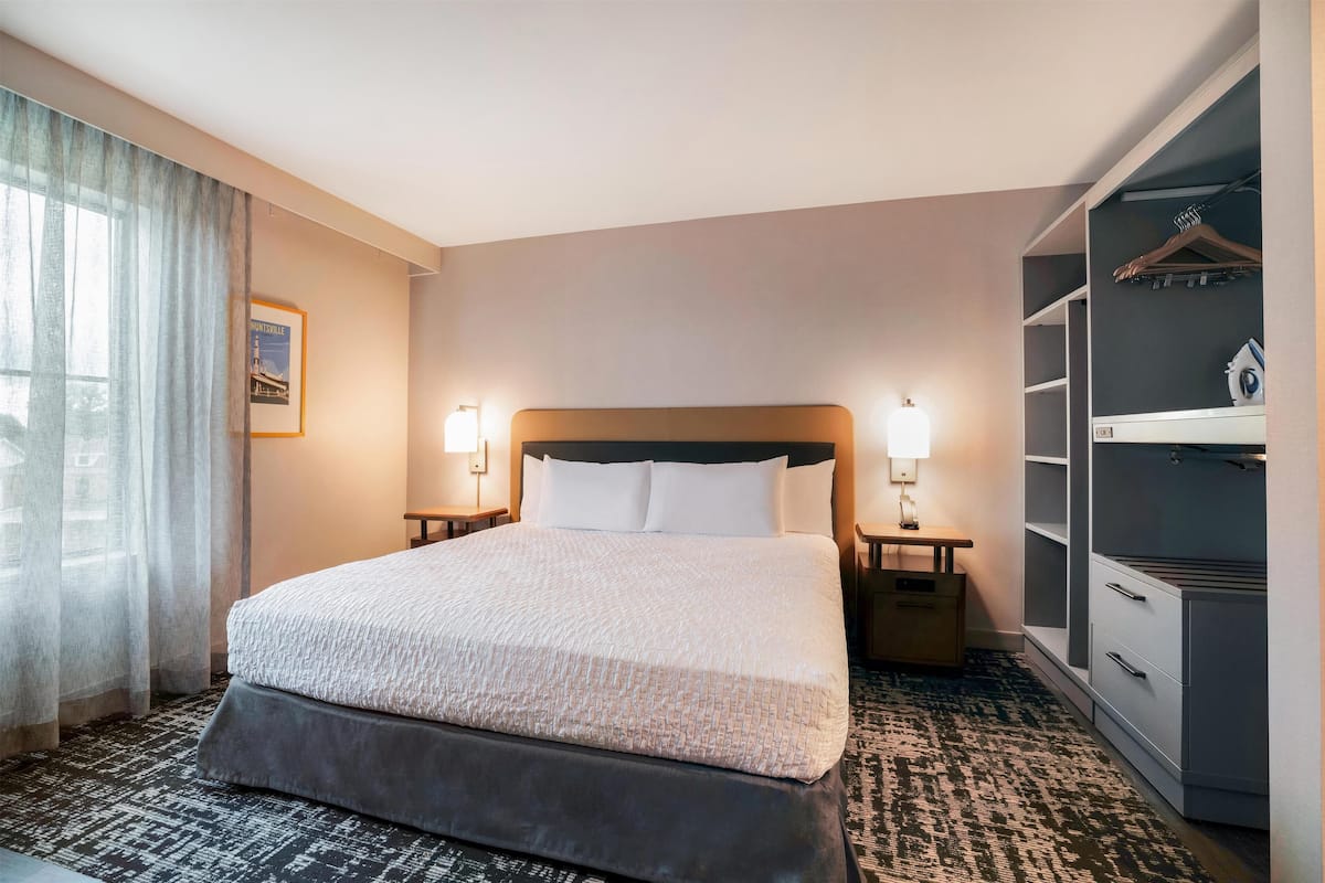 A neatly arranged hotel room with a large bed, bedside lamps, a wardrobe, and a framed picture on the wall.
