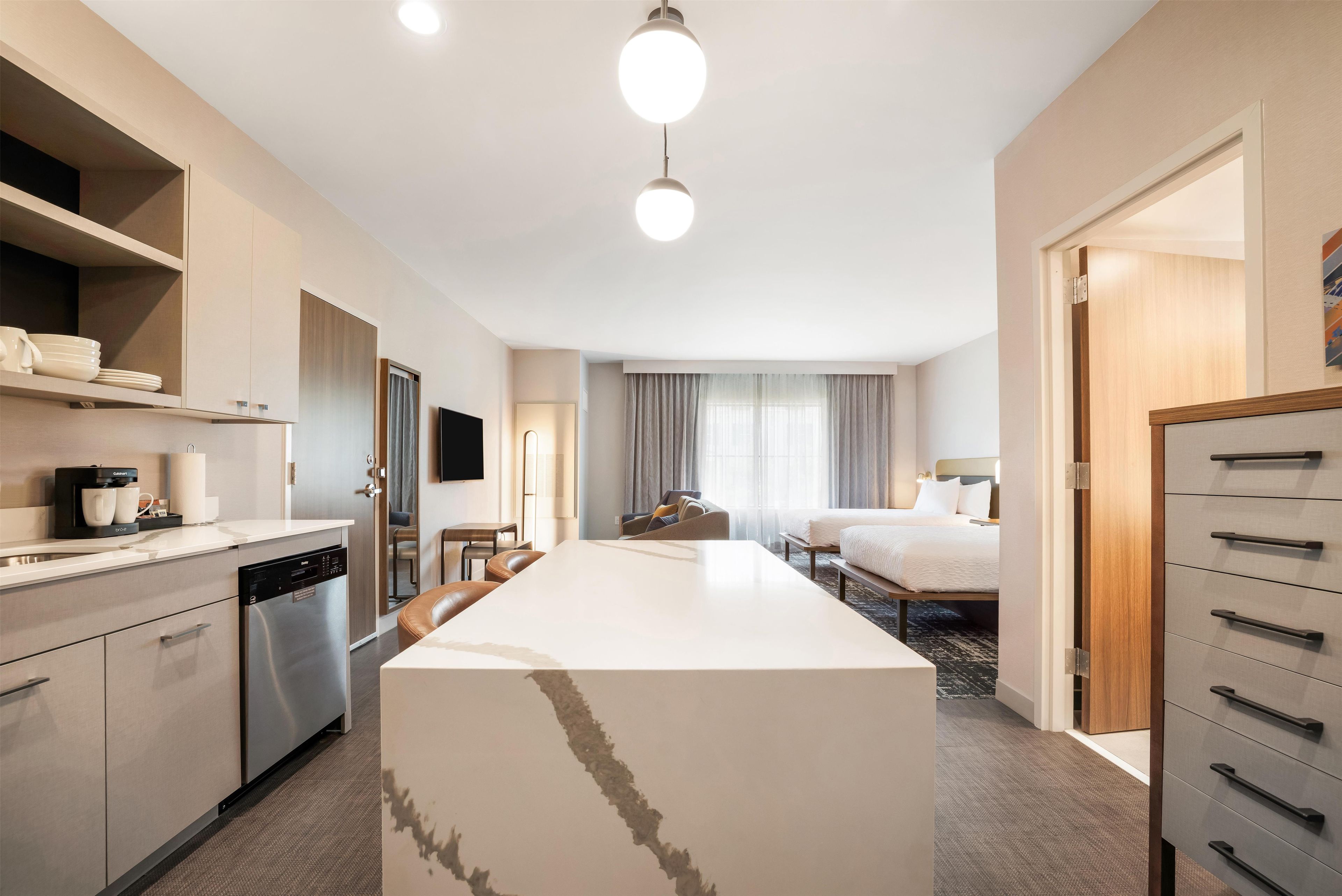A hotel room with a kitchenette, a dining area, a bed, and a bathroom.