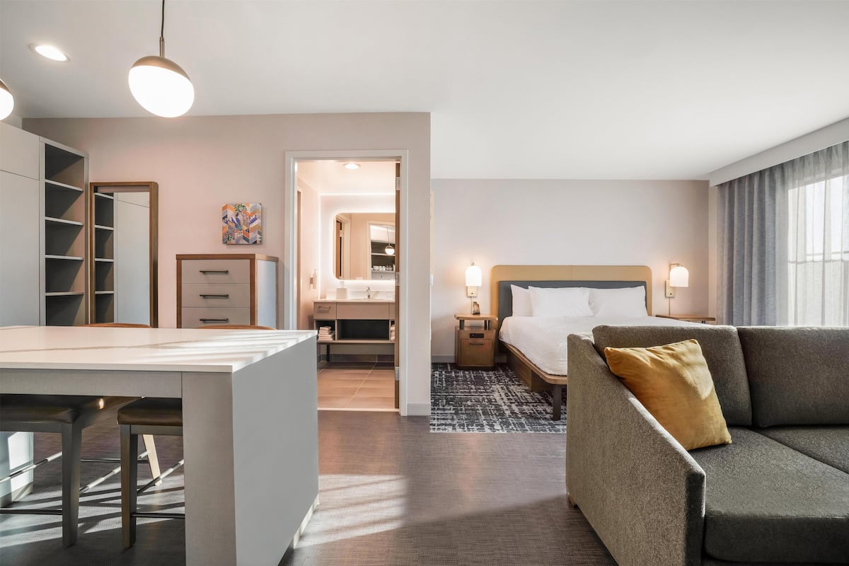 A modern hotel room with a desk, a sofa, a bed, and a bathroom.
