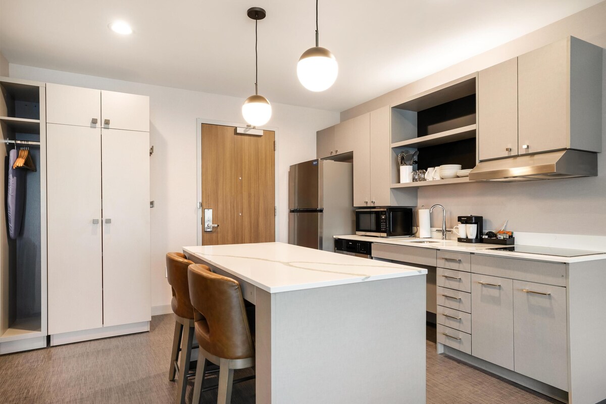 Una cocina moderna con una isla central, armarios blancos y electrodomésticos de acero inoxidable.