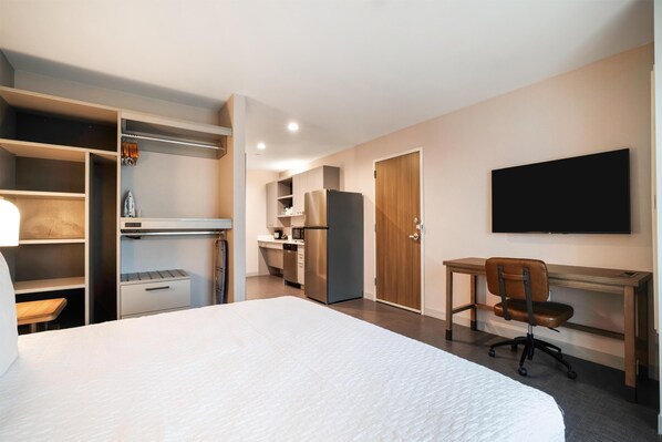 A hotel room with a bed, desk, chair, wardrobe, and kitchenette. - Homewood Suites By Hilton Madison Huntsville (Madison)
