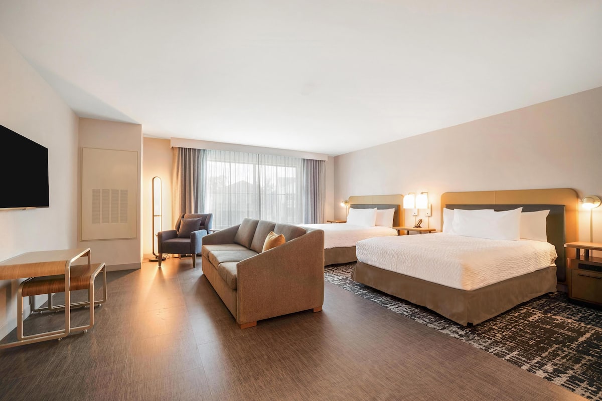 A hotel room with a bed, a sofa, a desk, and a TV.