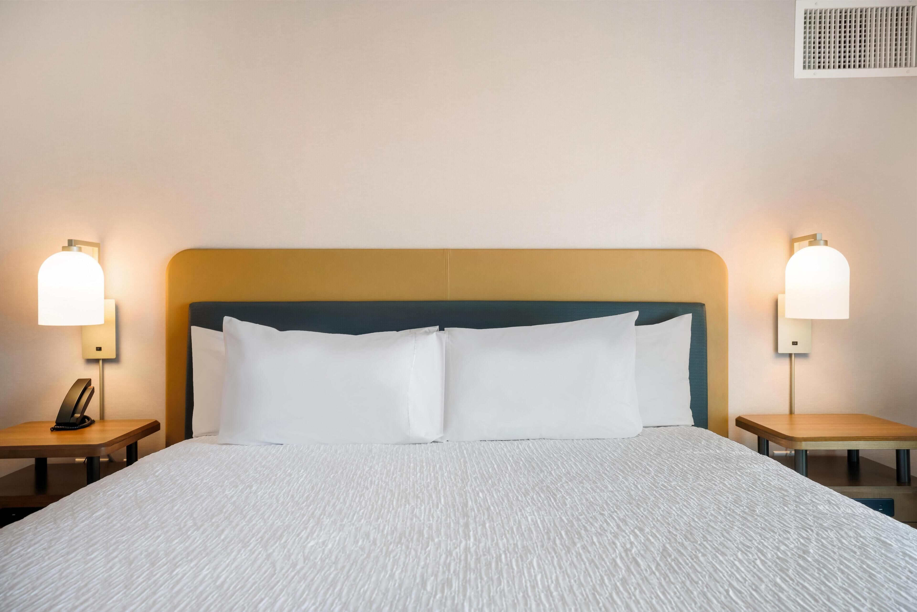 Una cama bien hecha con sábanas blancas, dos mesitas de noche con lámparas y un cabecero con un panel azul claro.
