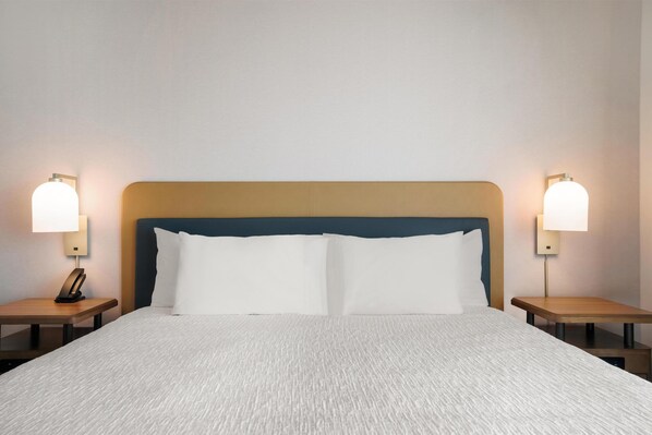 Una habitación de hotel con una cama grande, dos mesitas de noche y dos lámparas de pared.