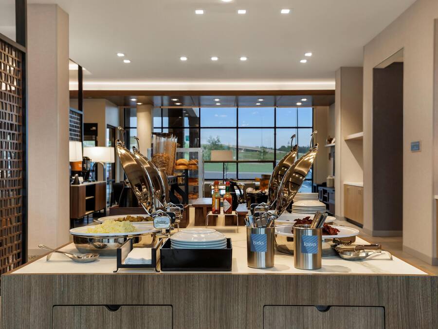 Un buffet proposant une variété de plats et d’ustensiles, une vue sur l’extérieur grâce à de grandes fenêtres et un aménagement intérieur moderne.