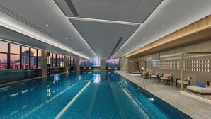 A modern indoor swimming pool with a city view, recessed lighting, and a lounge area with seating. - Hilton Yuyao (Ningbo)