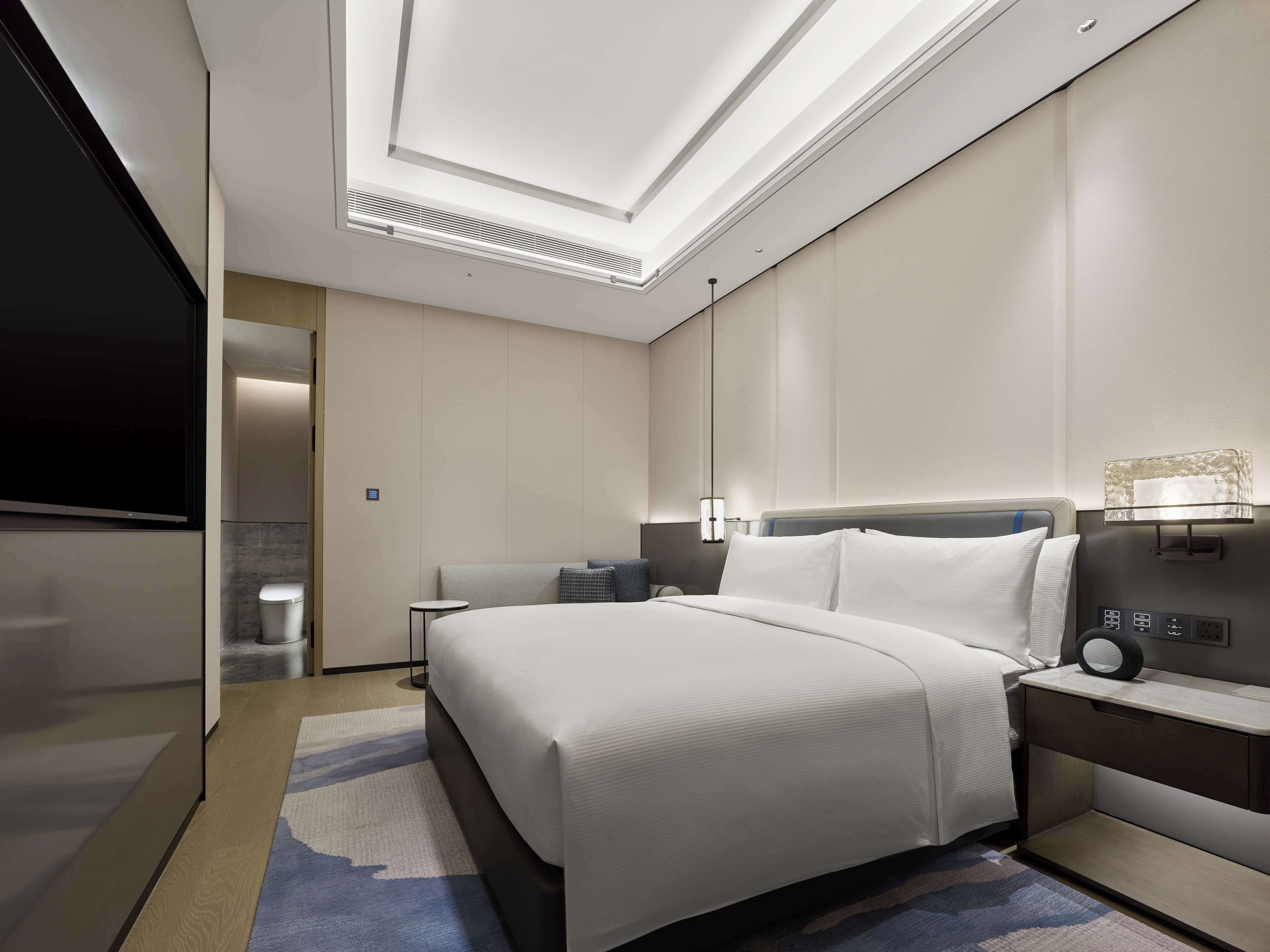 A modern hotel room with a large bed, bedside table, and a TV.