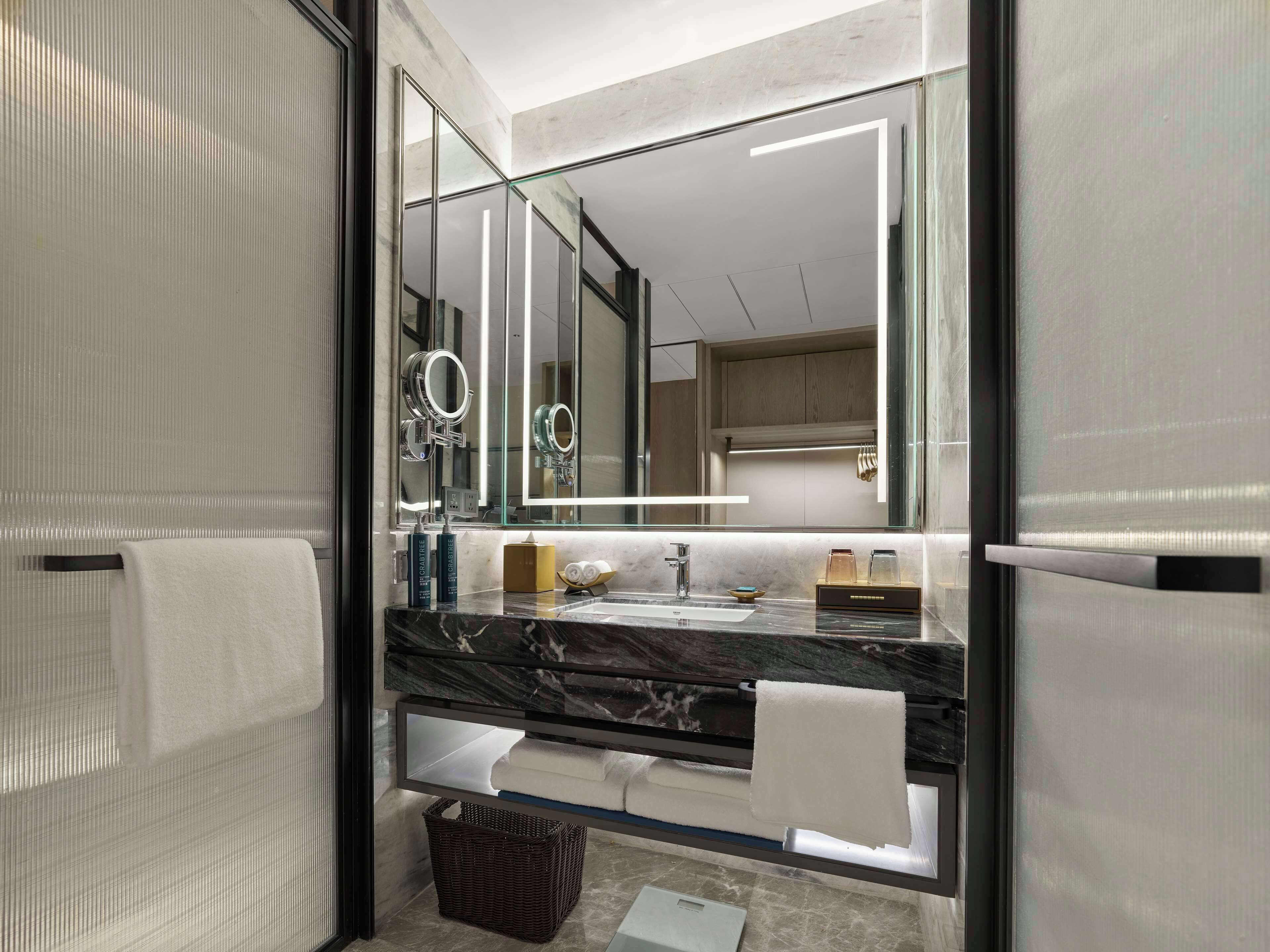 A modern bathroom with a glass partition, a marble countertop, a sink, a mirror, and a towel rack.