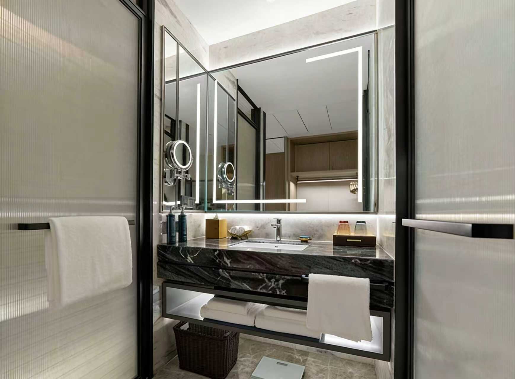 Un baño moderno con un espejo grande, encimera de mármol y lavamanos a la vista.