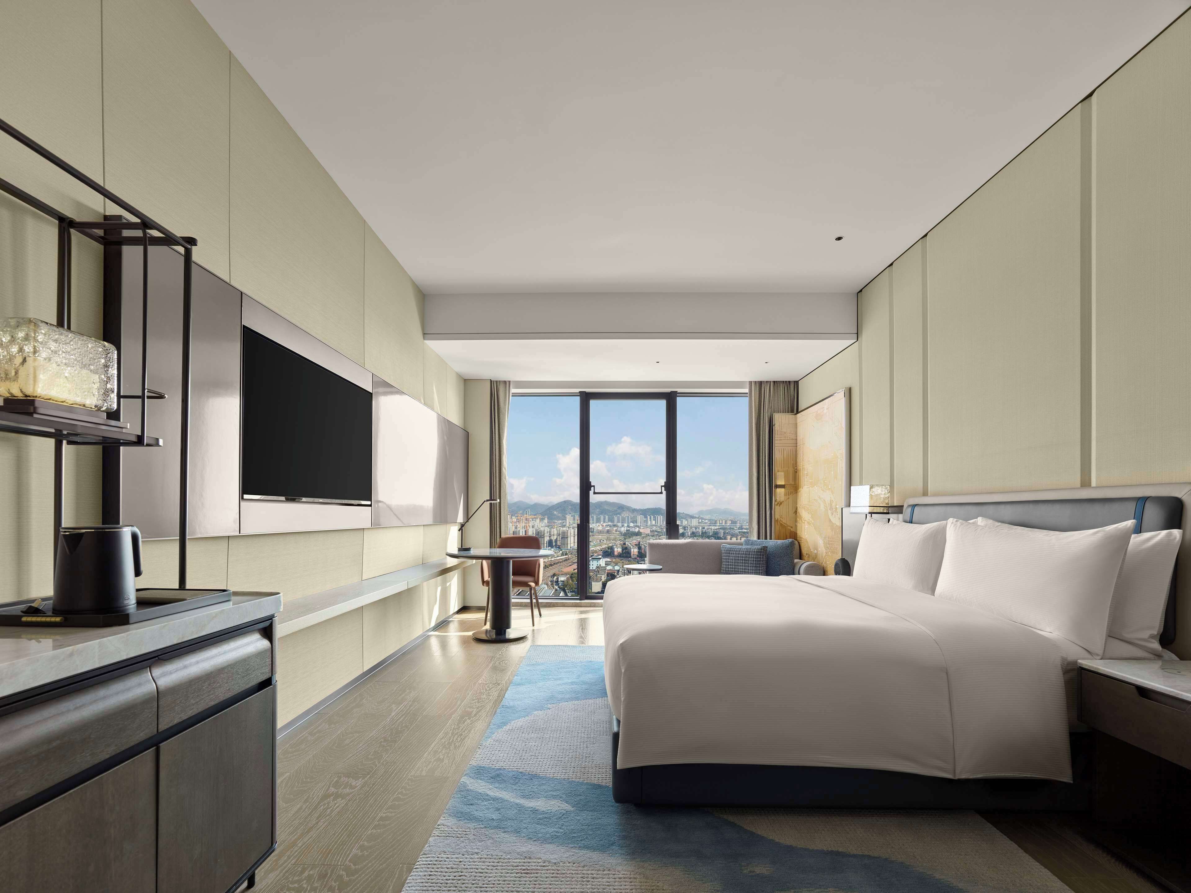 A modern hotel room with a large bed, a flat-screen TV, a coffee maker, and a city view.