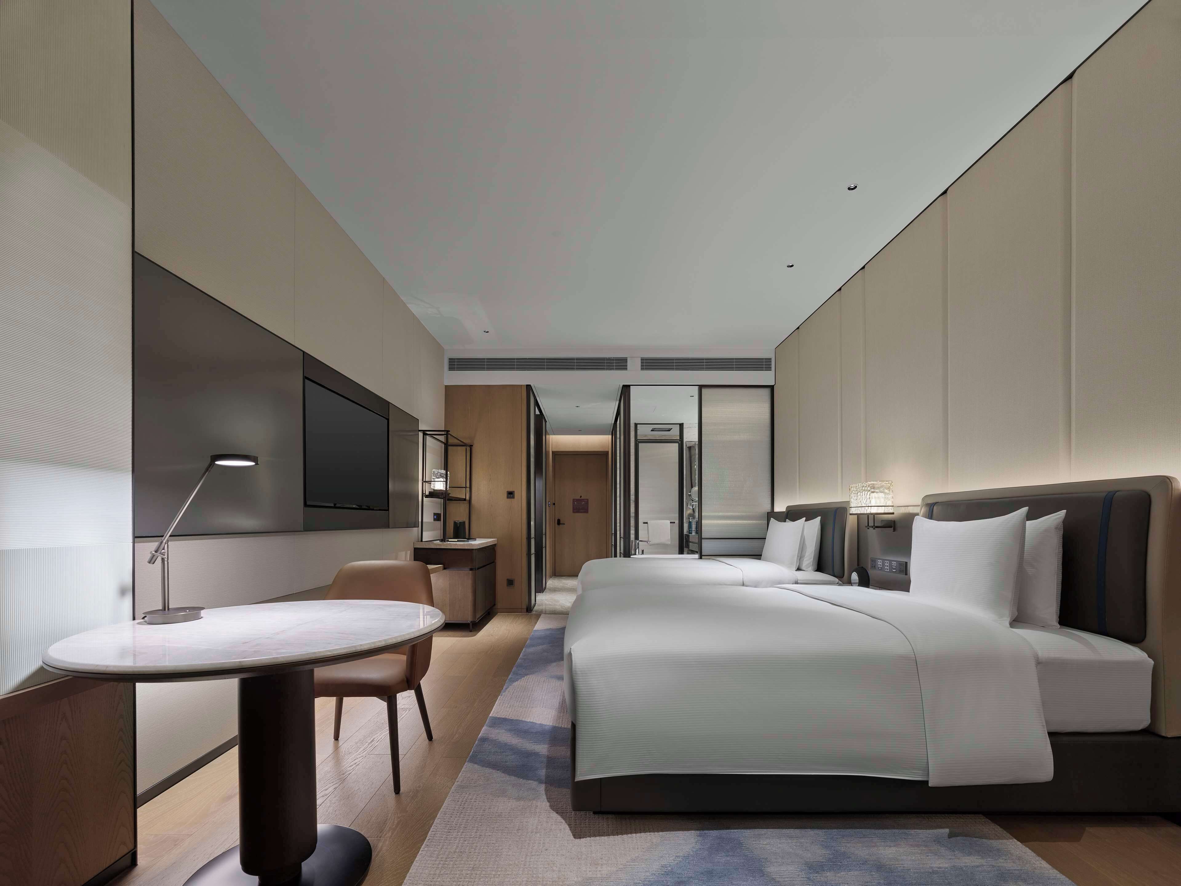 Ein modernes Hotelzimmer mit einem großen Bett, einem Schreibtisch mit Stuhl, einem an der Wand befestigten Fernseher und einem begehbaren Kleiderschrank.
