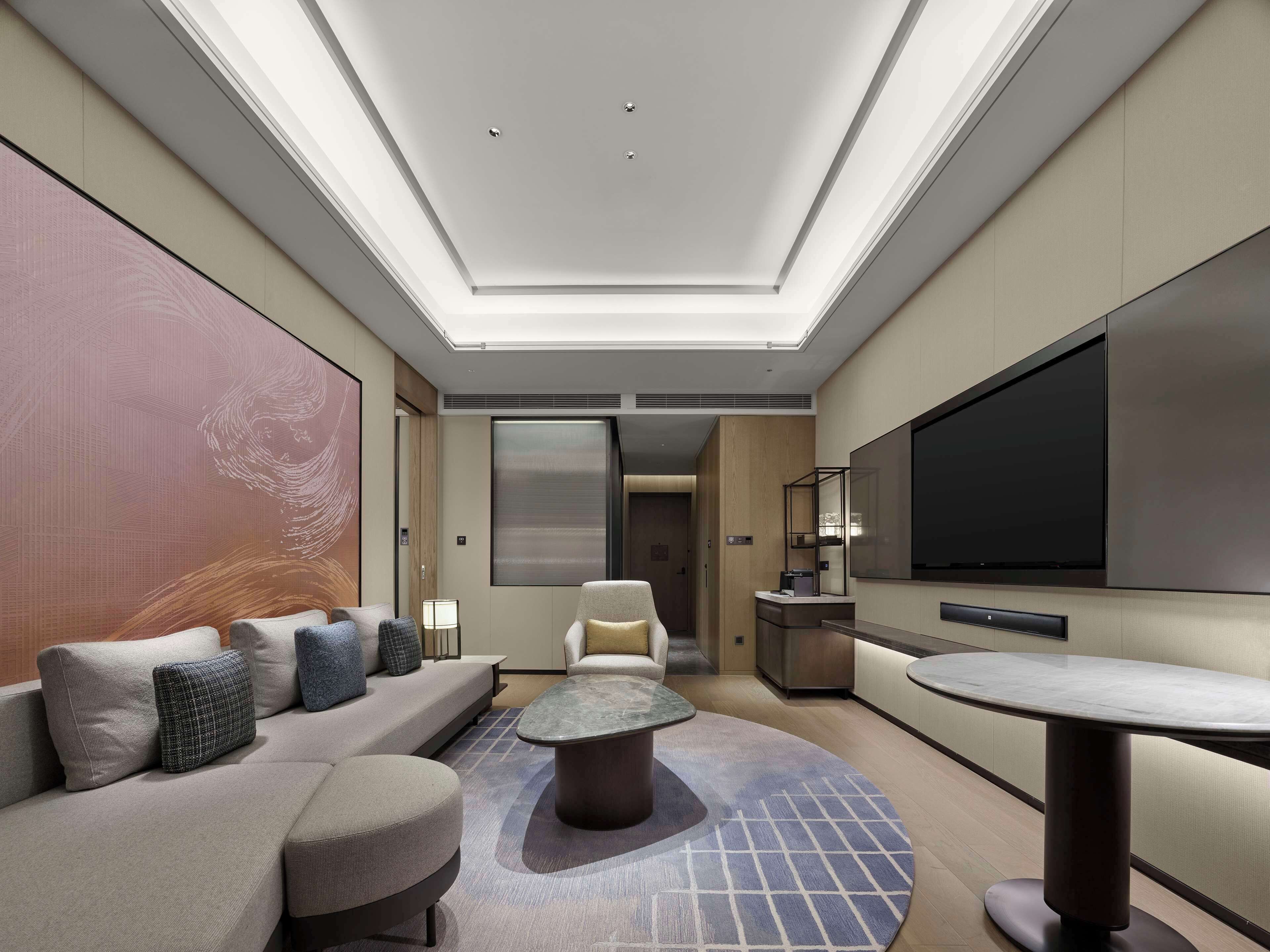 Ein modernes Hotelzimmer mit einem großen Bett, einem Sofa, einem Couchtisch, einem Fernseher und einer Decke mit Oberlichtern.