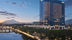 Un moderno hotel Hilton con fachada de vidrio, rodeado por una masa de agua y vegetación.