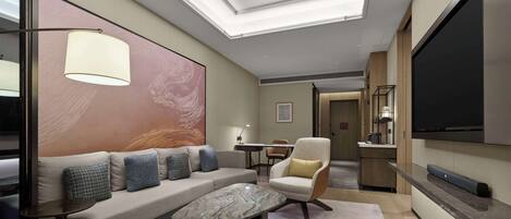 A modern hotel room with a sofa, armchair, and a flat-screen TV.