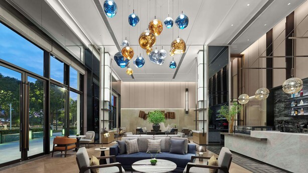 Un vestíbulo espacioso con diseño moderno, que incluye una zona de estar con sofás y sillones, una mesa de centro y un gran ventanal con vistas al exterior.