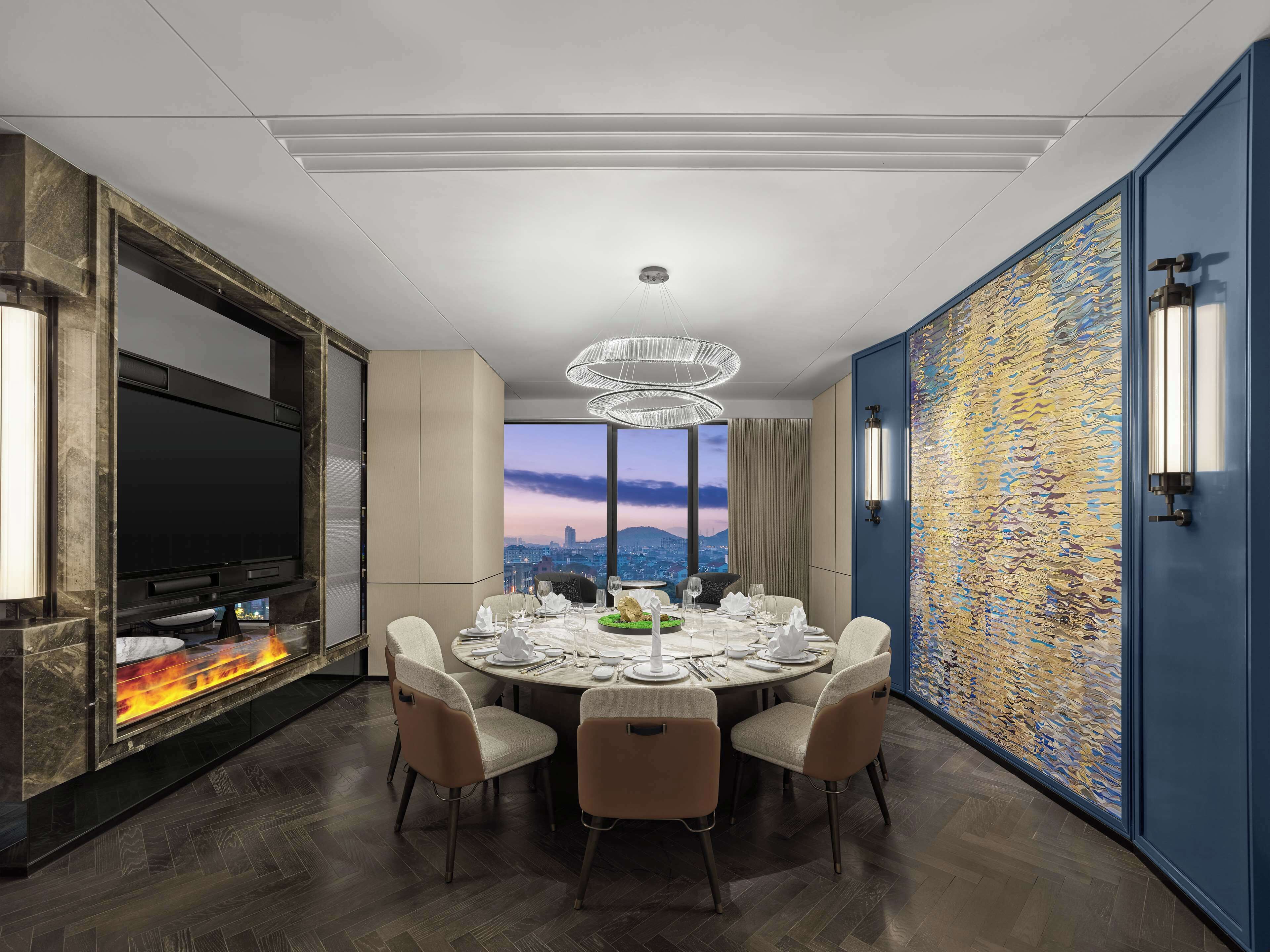 A modern dining room with a round table, six chairs, a fireplace, and a city view.