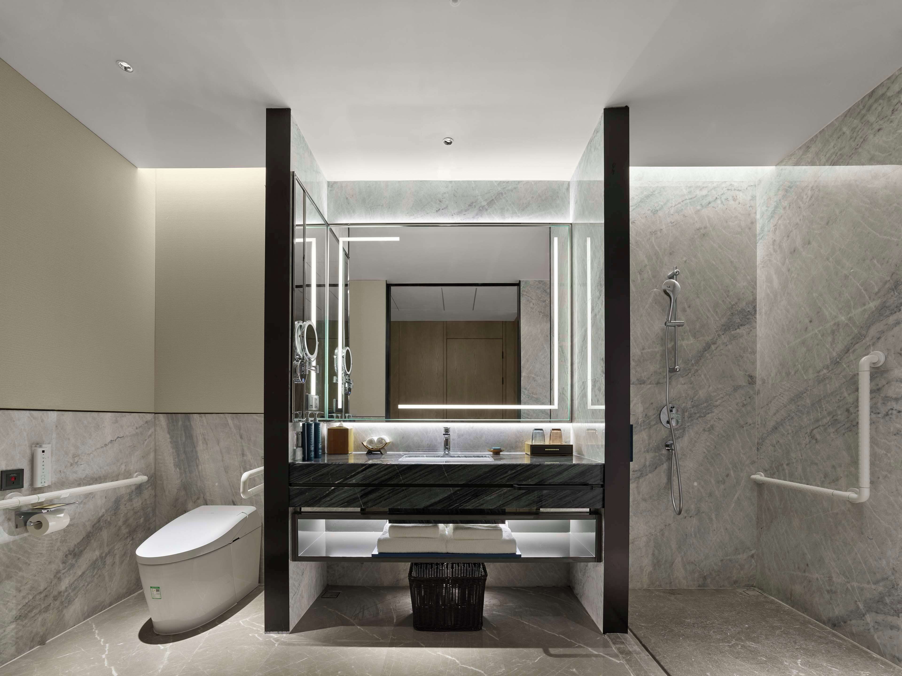 Une salle de bain moderne avec un sol en marbre, un meuble-lavabo entouré de parois en verre, des toilettes, une douche et un grand miroir.