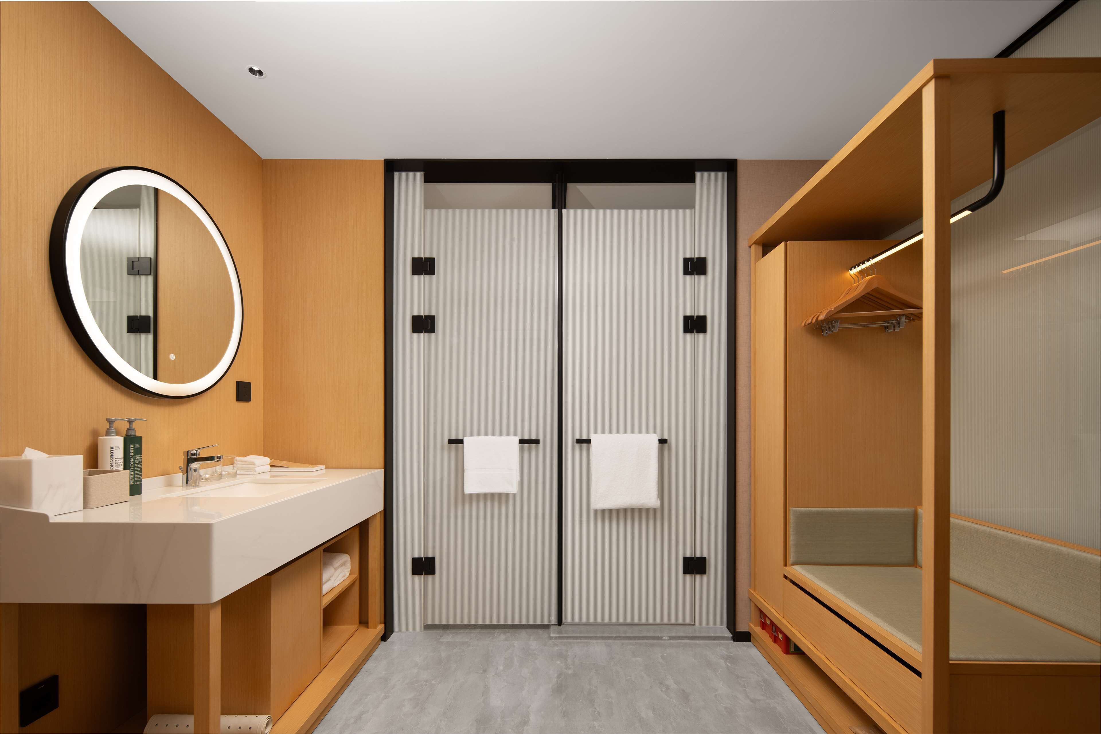 Un baño moderno con tocador, espejo y vestidor con banca.