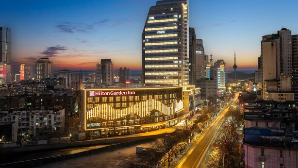 Un hôtel moderne doté d’une façade en verre remarquable et d’une enseigne lumineuse, situé au cœur d’un paysage urbain au crépuscule.