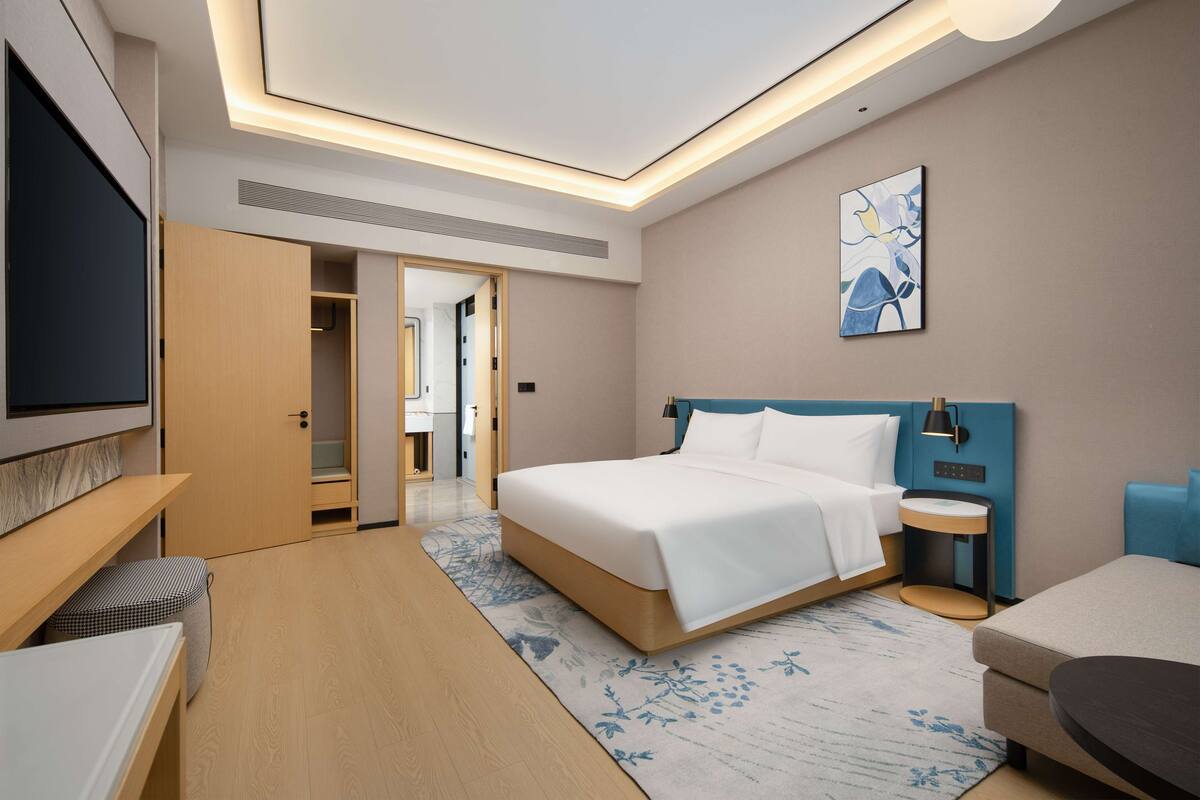 Une chambre d’hôtel moderne avec un grand lit, une table de chevet, une télévision et un petit coin salon.