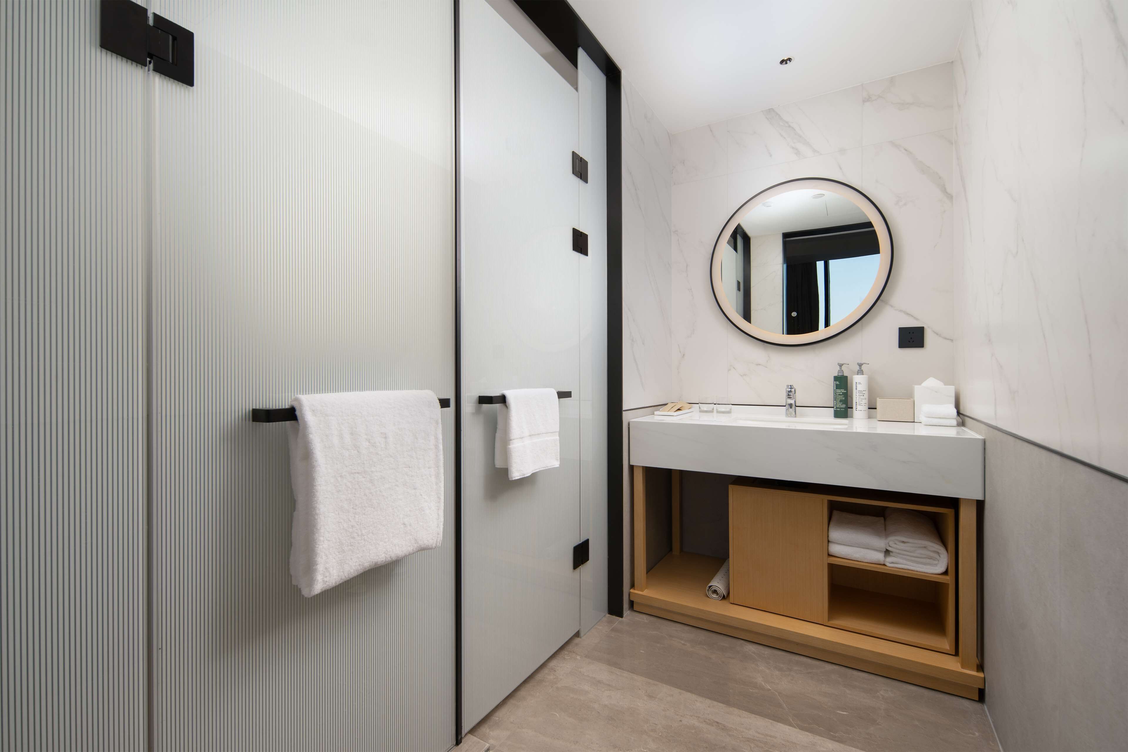 A modern bathroom with a large mirror, white towels, and a marble countertop.