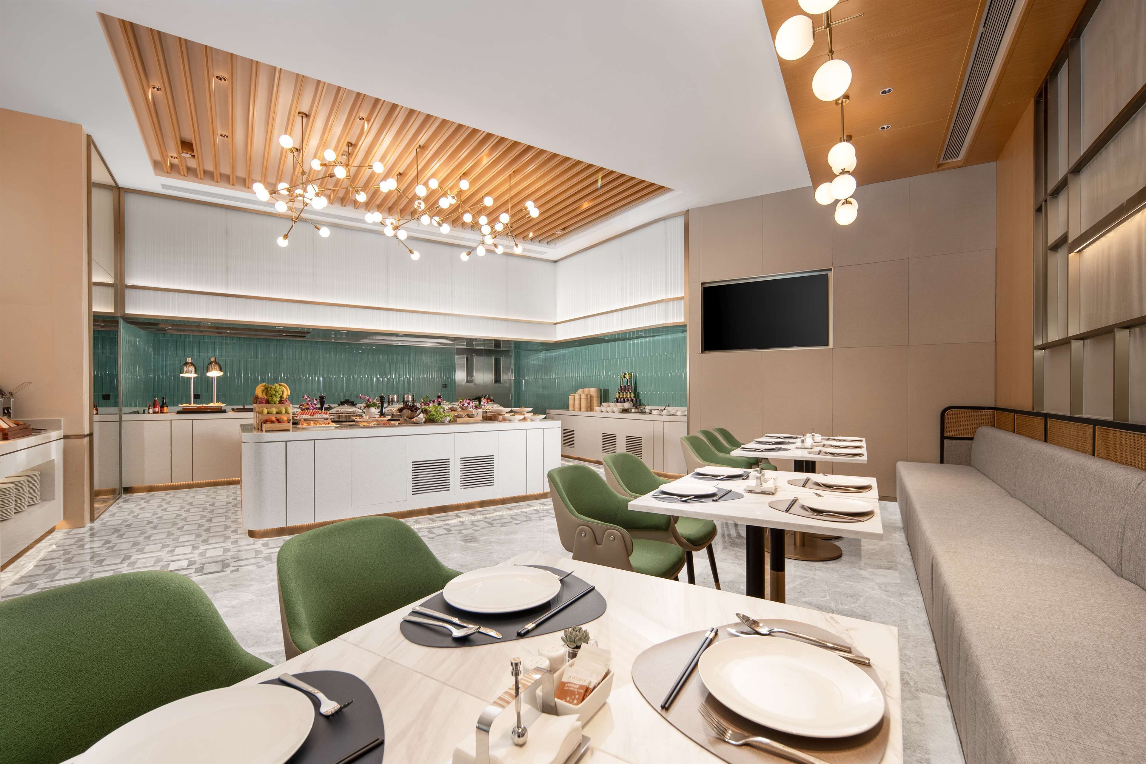 A modern dining area with a central island, green upholstered chairs, and a long table set for a meal.