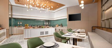 A modern dining area with a central island, green upholstered chairs, and a long table set for a meal.