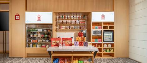 Una tienda con estantes llenos de botanas y bebidas, una sección refrigerada y una mesa expositora con productos envasados.