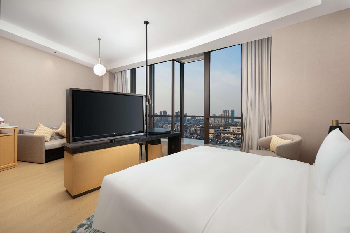 Ein modernes Hotelzimmer mit einem großen Bett, einem Flachbildfernseher, einem Schreibtisch und Blick auf die Stadt.