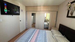 Ein Schlafzimmer mit einem Bett, einem an der Wand montierten Fernseher, einem Kleiderschrank und einem Spiegel.
