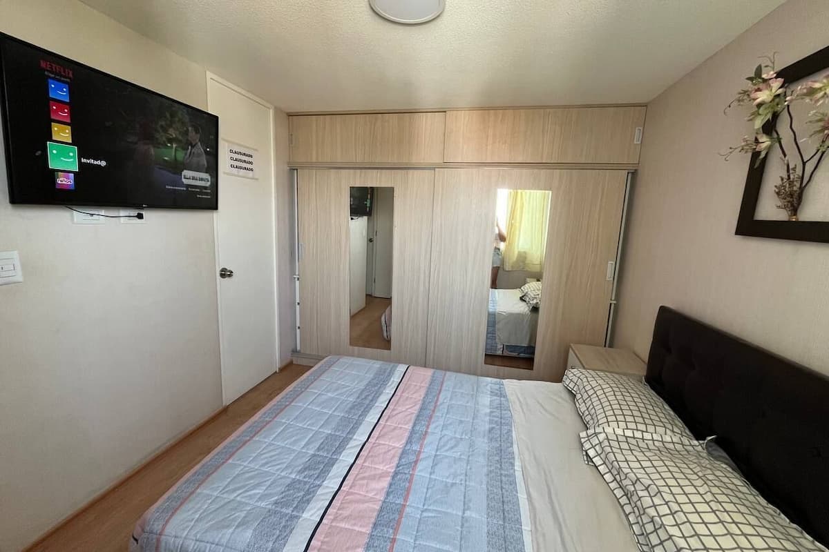 Ein Schlafzimmer mit einem Bett, einem an der Wand montierten Fernseher, einem Kleiderschrank und einem Spiegel.