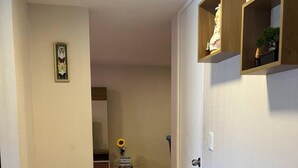 Ein Flur mit Holzboden, einer Tür mit Griff und einem kleinen Tisch mit einer Vase und einem Sonnenblume.