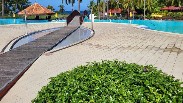 A pool area with a wooden deck, palm trees, and a clear blue sky. - Au Beau Village Studio Nature View (Sainte-Luce)