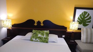 A hotel room with a large bed, two bedside lamps, a wooden headboard, and a framed tropical leaf artwork on the wall. - Au Beau Village Studio Nature View (Sainte-Luce)