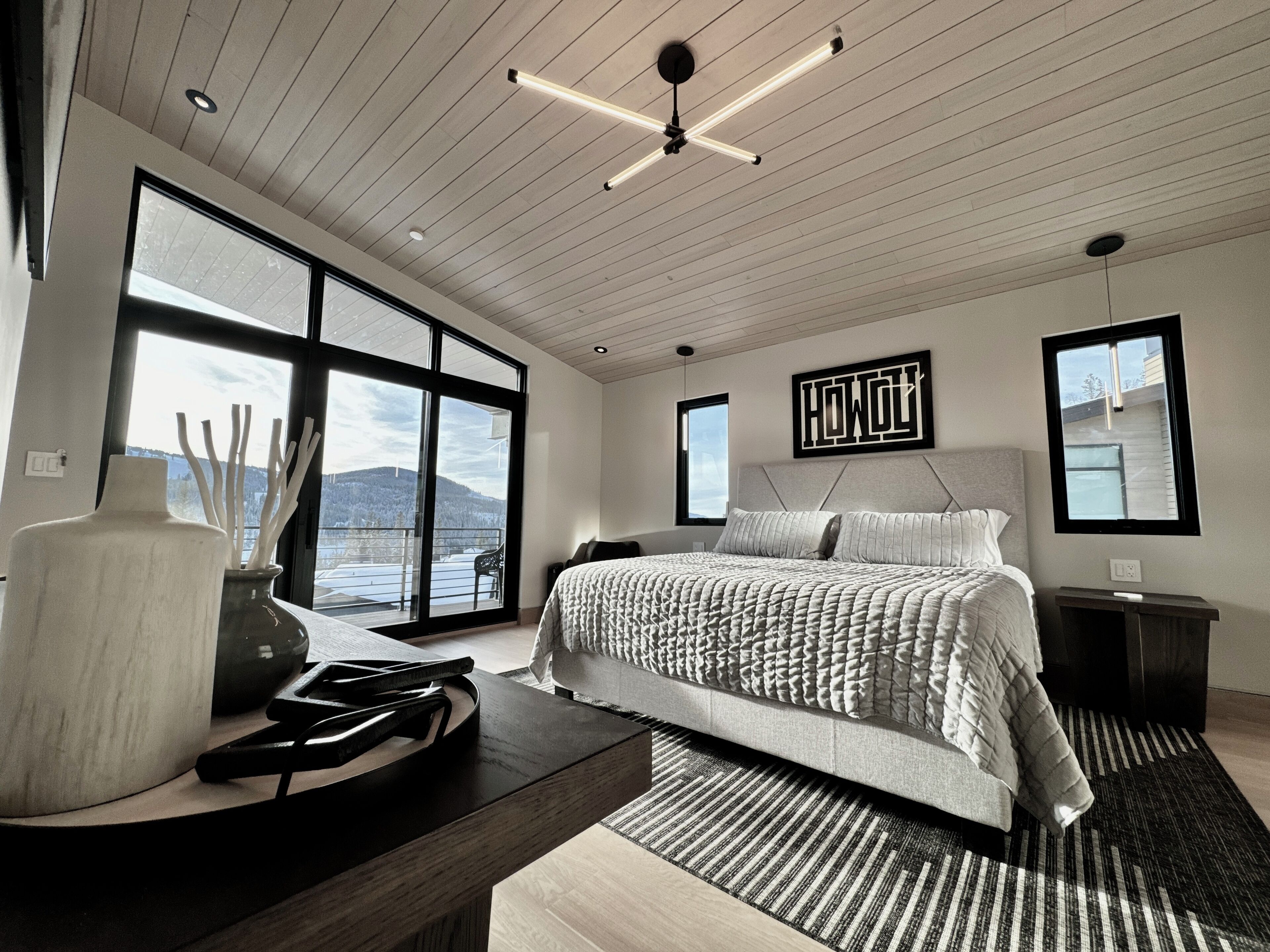 A modern bedroom with a large bed, a view of the outdoors, and a ceiling fan.