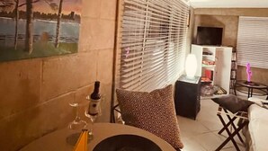 Una zona de estar acogedora con un cuadro en la pared, una mesa con una botella y copas, y un televisor sobre un mueble.