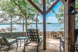 A covered outdoor seating area with stone walls and metal furniture, overlooking a lake with docks.
