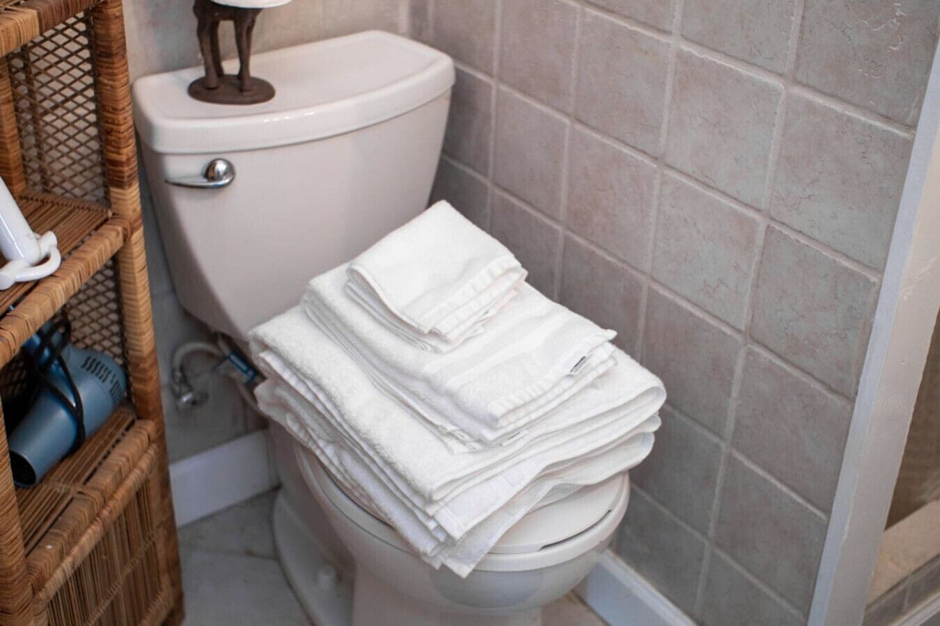 Et badeværelse med toilet, en kurveskuffe med toiletartikler og en stak hvide håndklæder.