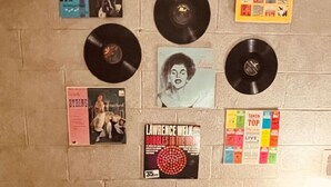 Una habitación con una pared de ladrillo gris, un sofá de cuero negro con detalles blancos y varios discos de vinilo y carteles expuestos en la pared.
