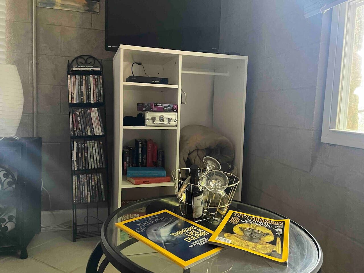 A room with a glass table displaying magazines, a bookshelf with DVDs, and a decorative skull.