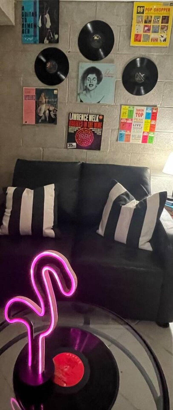 A living room with a black sofa, a neon sign, and vinyl records on the wall.