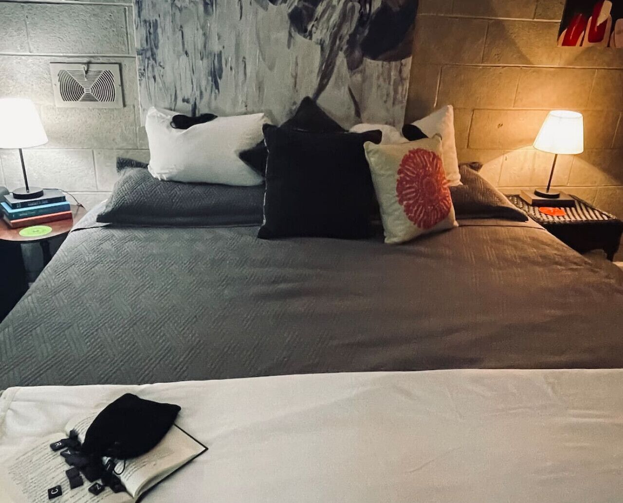 A neatly made bed with a white pillow and a black pillow, a book, and a pair of black shoes on the bed.
