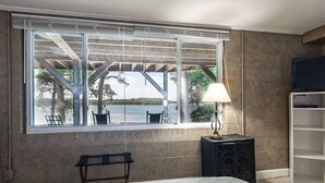 Un dormitorio con un ventanal grande, una cama, un banco, una lámpara y un mueble para televisión.