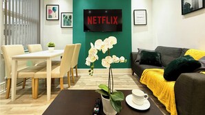 Una sala de estar moderna con un letrero de Netflix, un comedor con una mesa y sillas, y un sofá con una manta amarilla.